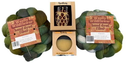 Two skeins of green hand-dyed fiber with Speakeasy packaging on a gray background