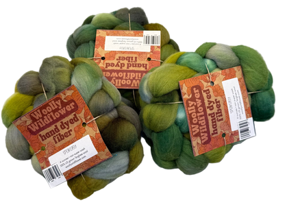 Three skeins of green hand-dyed fiber with labels on a gray background